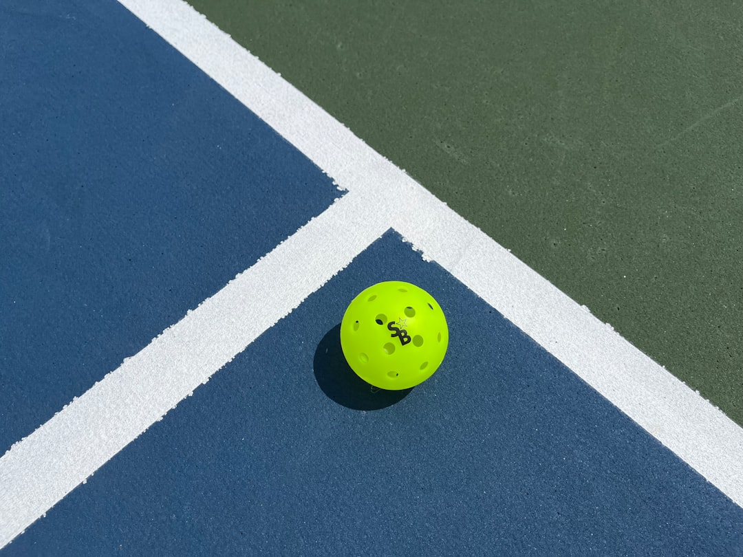 Bola pickleball kuning cerah di atas lapangan hijau biru